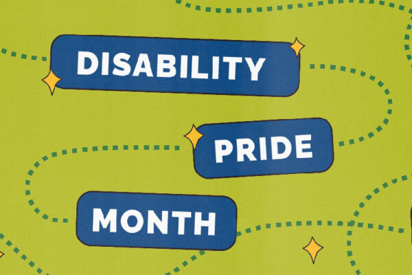 A baby photo of Mark, in a bathroom, posing with his arm on his hip and his other arm on his shoulder with his legs crossed and inverted. He has short black hair and is wearing black shorts, a navy and pink shirt, and black shoes.