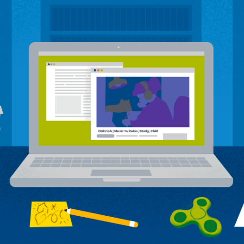 Laptop sitting on a desk, surrounded by books, papers, coffee, a fidget spinner, and headphones, denoting a study space.